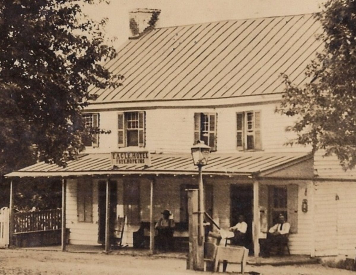 The two-story hotel with Eagle Hotel signed above the porch, men gathered along it and a hand pump at the curb.