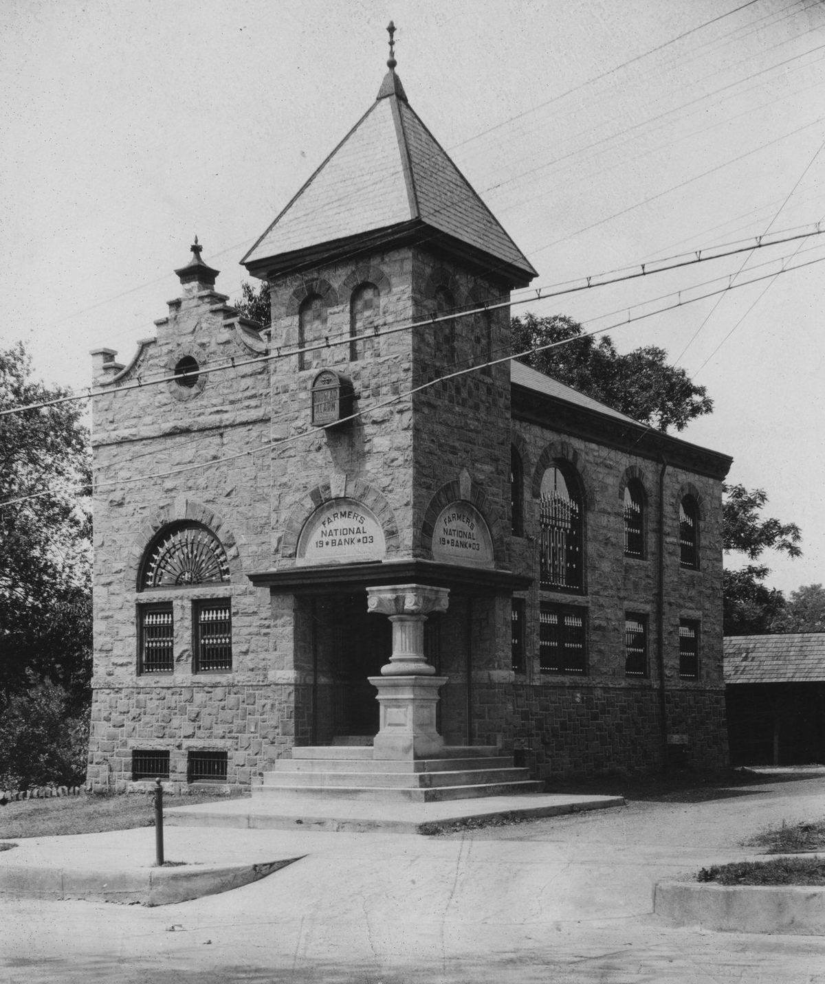 The stone bank alone on its corner: squat corner tower, arched entrance, stepped Flemish gable.