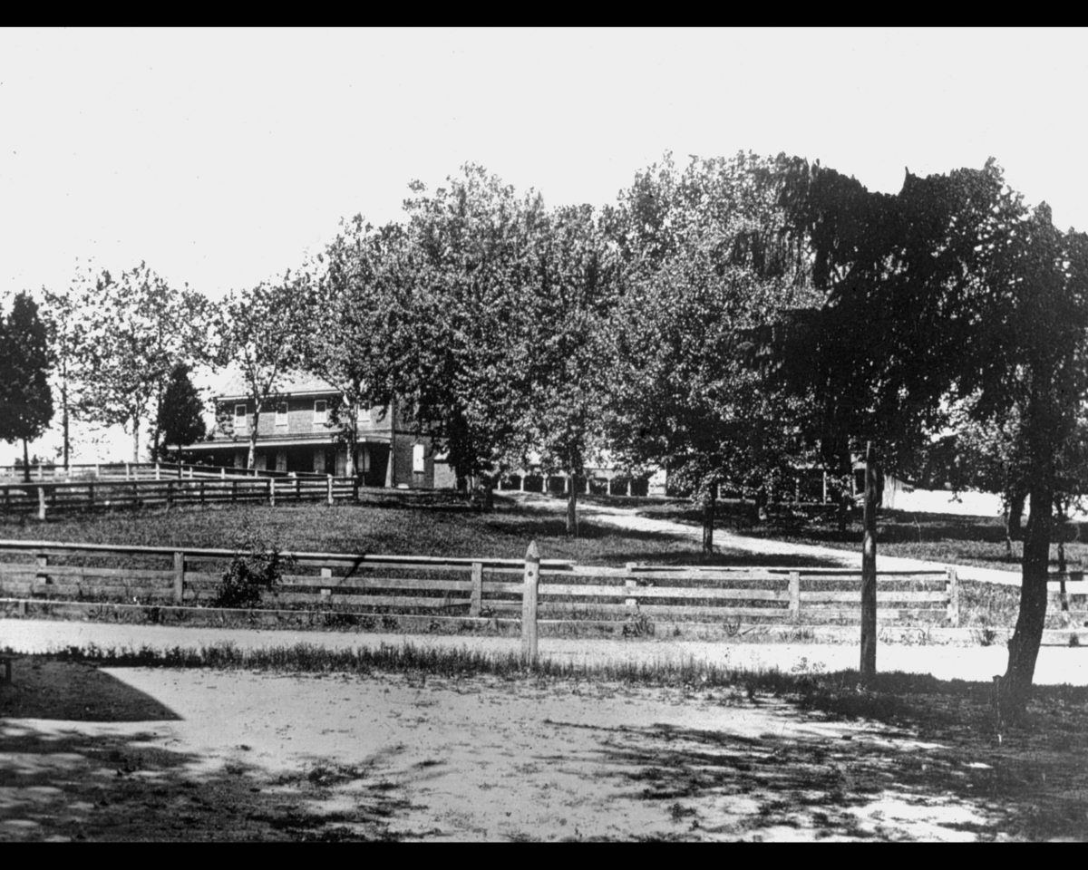 The meeting house nearly hidden in trees beyond a rail fence, a porch-fronted farmhouse at left.