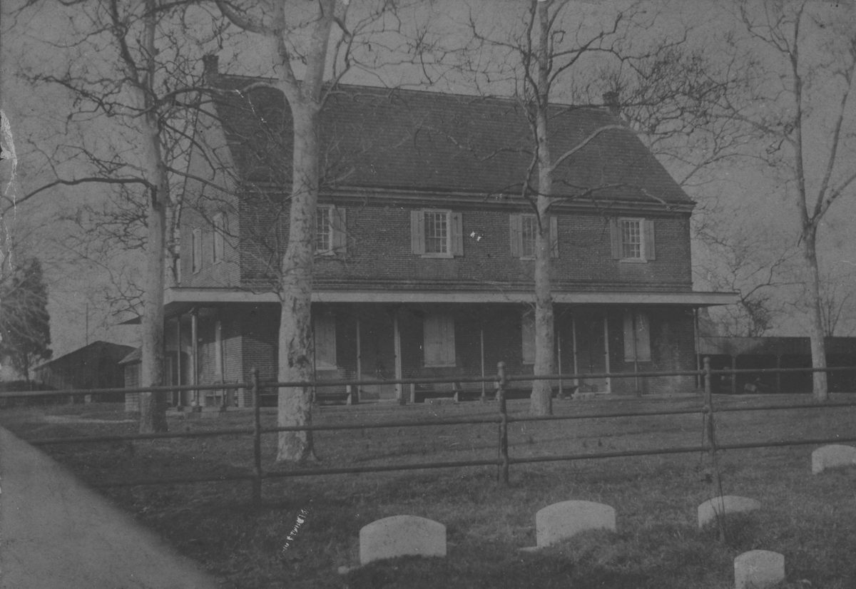 The brick meeting house and its long porch behind bare trees, low gravestones in the grass before it.