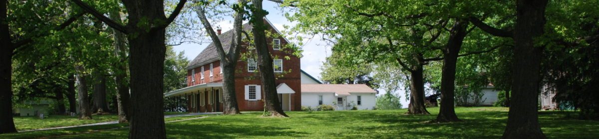The brick meeting house today under old shade trees, its lawn open to the corner.