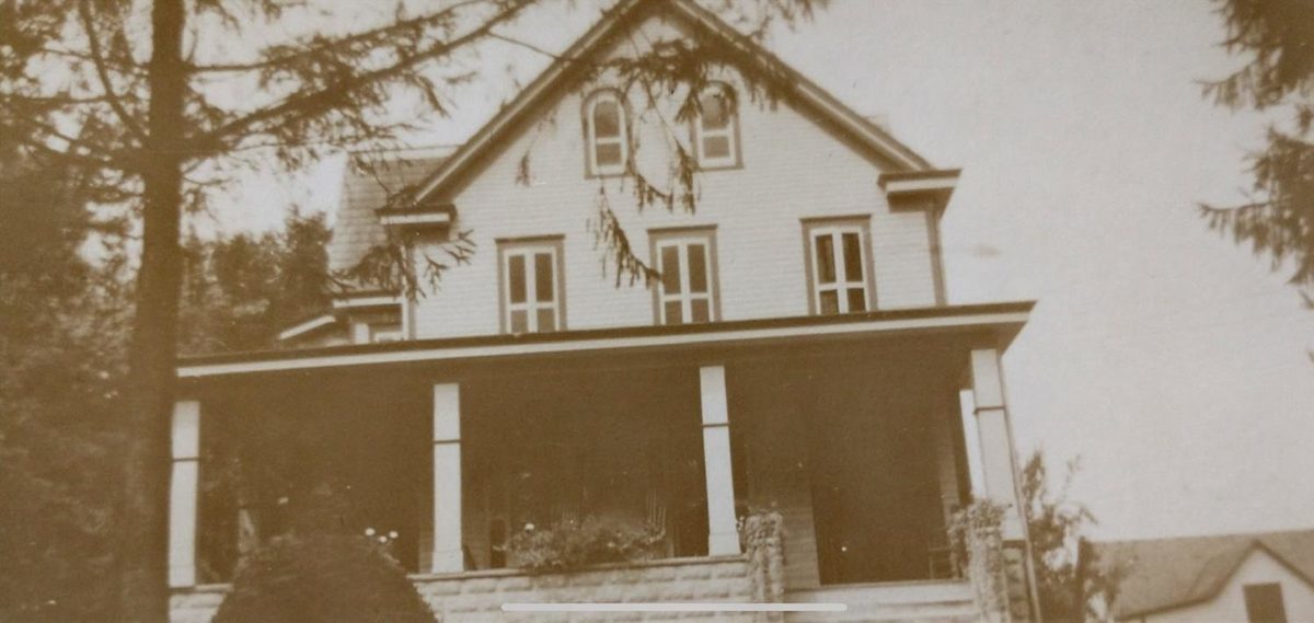 The tall frame house with two arched windows in its top gable, seen past a tree over the porch roof.