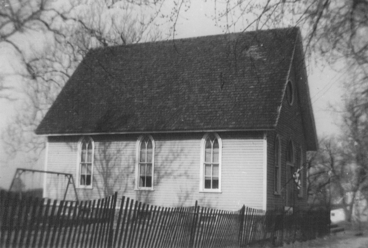 The white frame church gable-on to the street, pointed windows down its side, behind a low fence.