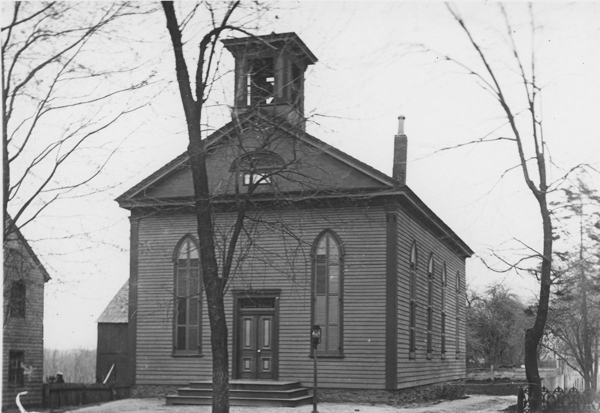 The clapboard church with its front cupola and long pointed windows, bare trees around it.