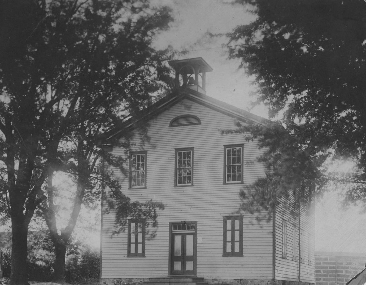 The two-story schoolhouse with twin front doors and a bell cupola centered on its roof.