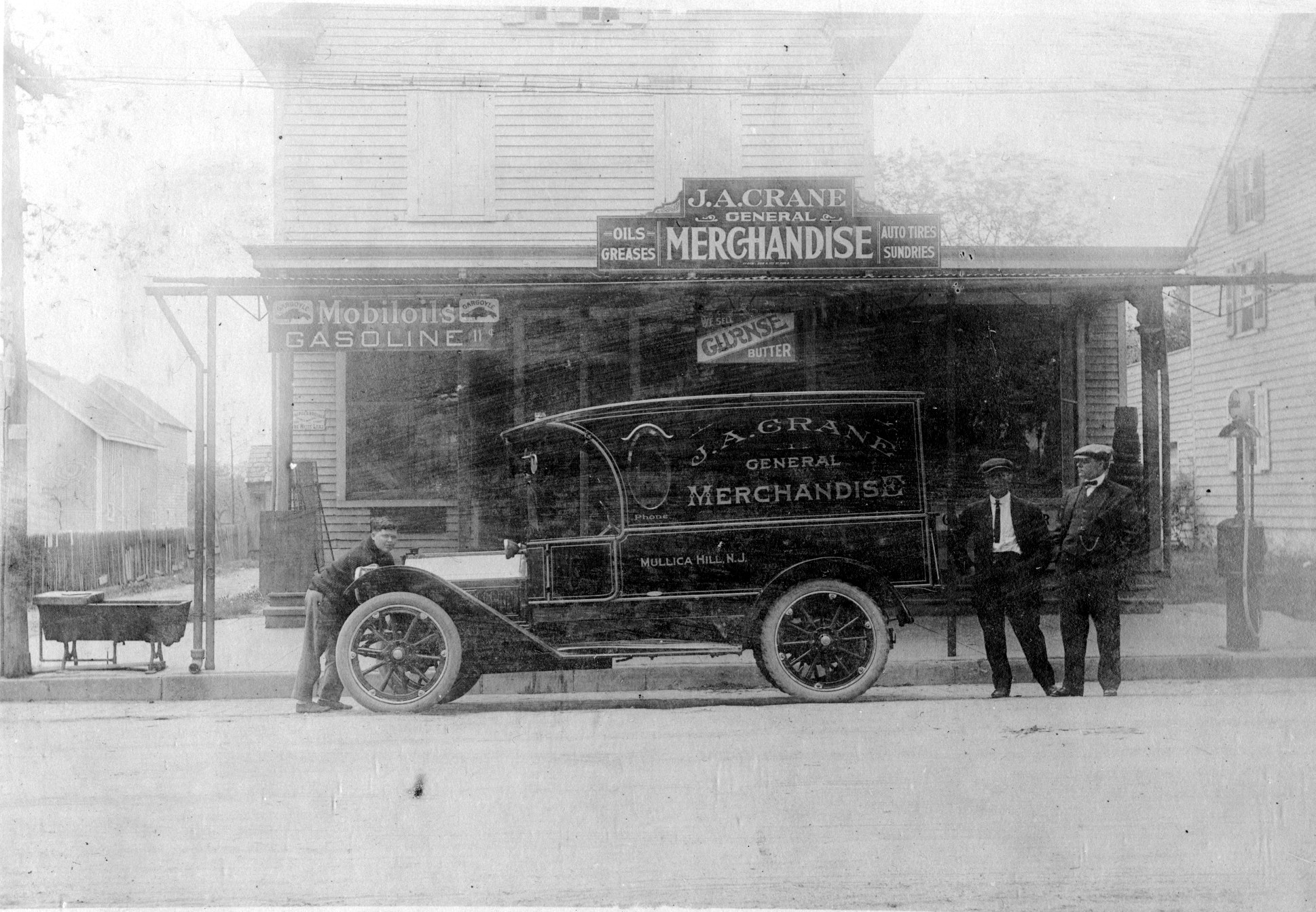 A boxy delivery truck lettered J. A. Crane General Merchandise, Mullica Hill, N.J., parked before the store porch, the signs above offering oils, greases, auto tires, and gasoline at eleven cents.