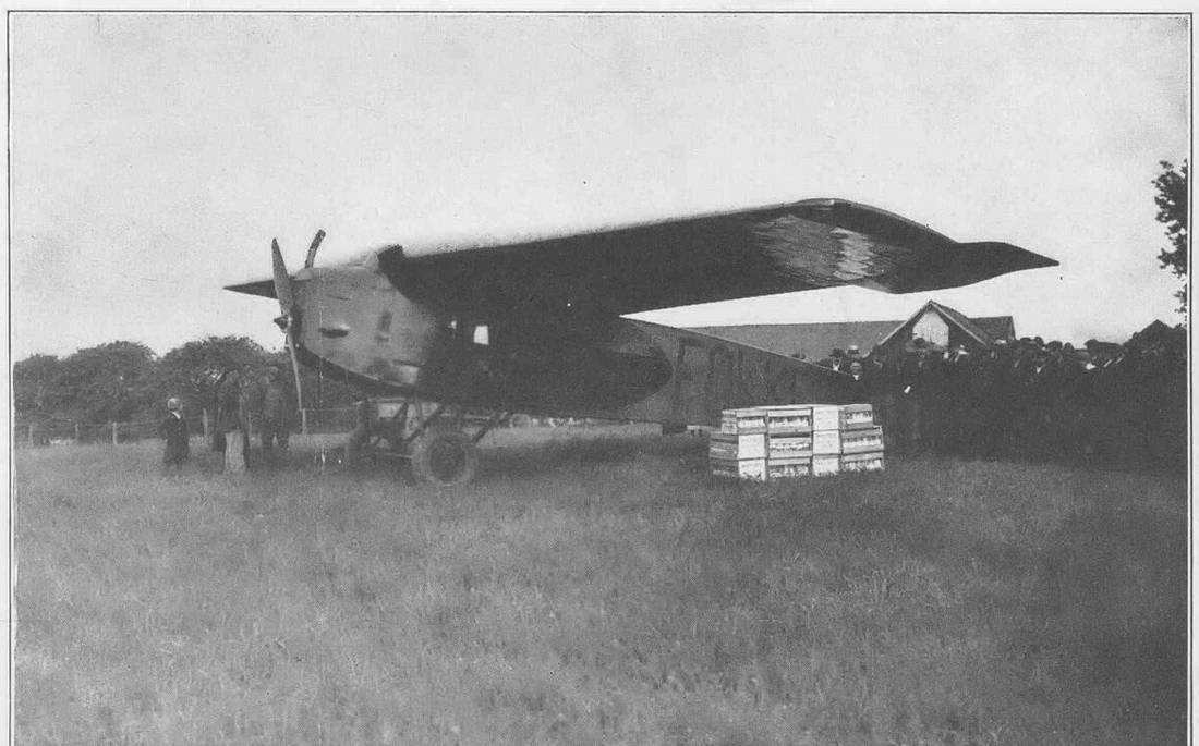 The high-winged monoplane parked in a field, wooden crates stacked beside its cabin.