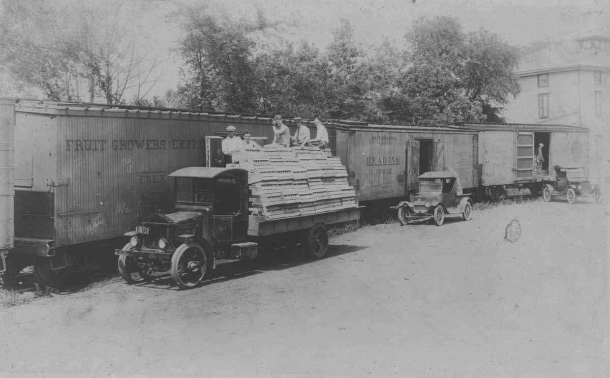 Crates riding a conveyor from a truck into a boxcar lettered Fruit Growers Express, men working on top.