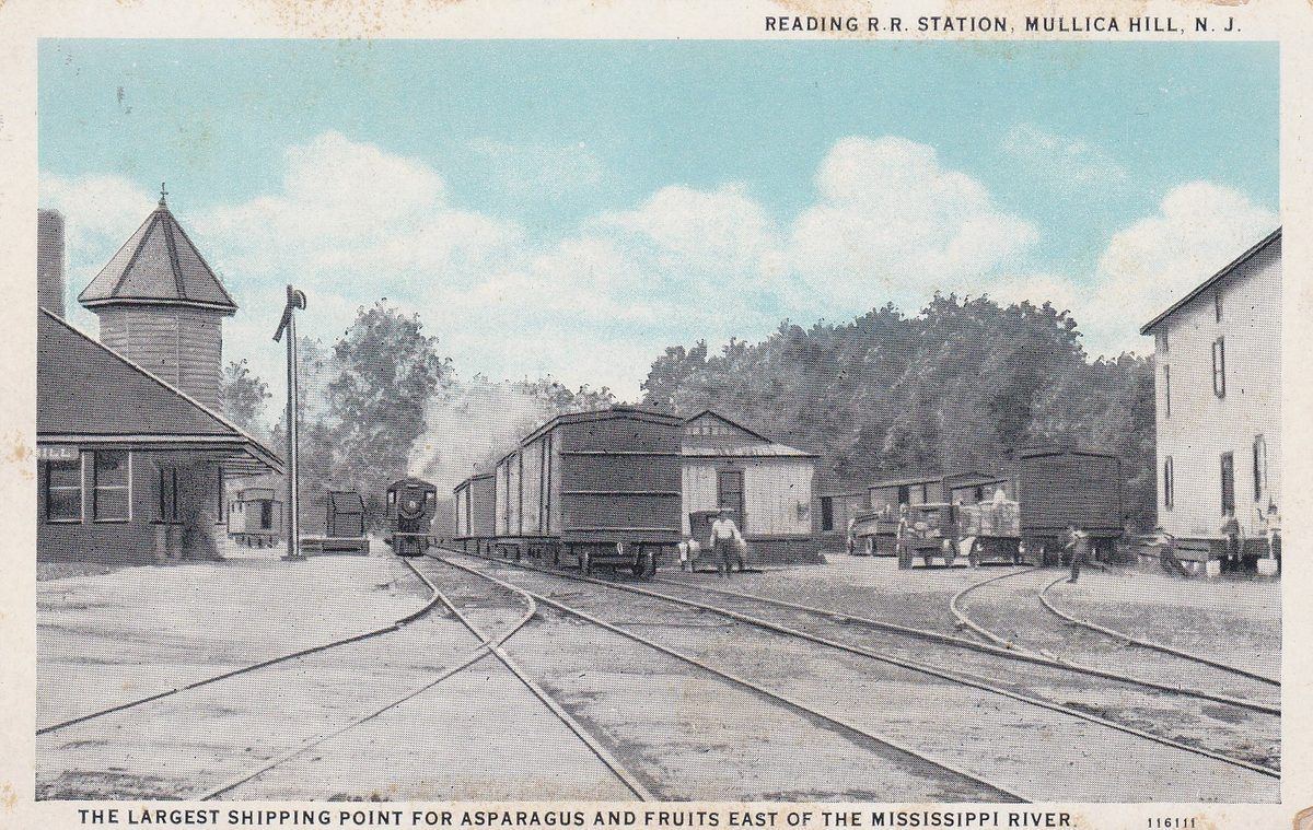 A tinted postcard of the railroad station yard, a train arriving past the water tower, a printed caption along the bottom.