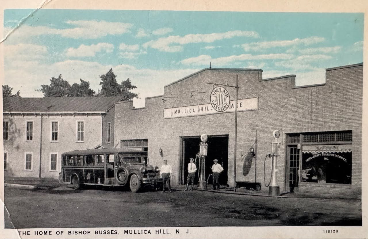 A tinted postcard of the brick garage with a stepped parapet, a round Sinclair Gasoline sign over the open bay, a bus and gas pumps out front, and a printed caption along the bottom.